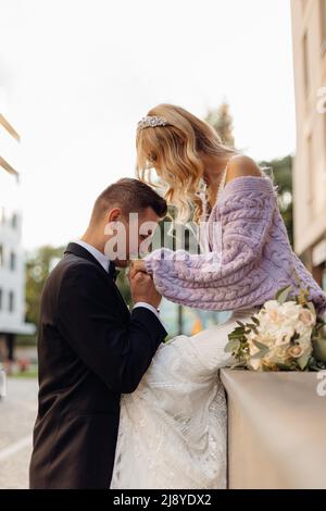 Beautiful young wedding couple in black suit and white dress walk around city, kiss and enjoy on street background. Portrait of happy bride with Stock Photo
