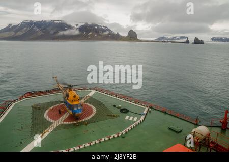 A helicopter on the rear of the 50 Years Of Victory (50 Let Pobedy) nuclear icebreaker with Cape Tegethoff, Hall Island, Franz Josef Land, behind Stock Photo