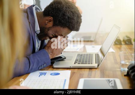 Tired black businessman with headache working in office Stock Photo