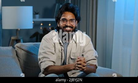 Close up happy indian arabian bearded man football male fan sitting at home evening at TV screen in dark living room and watching online match celebra Stock Photo