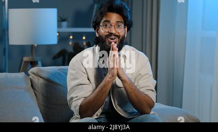 Arabic happy motivated man watching TV at home at night late in evening. Spaniard bearded Indian guy millennial male fan of favorite sports team rejoi Stock Photo