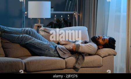 Exhausted overloaded arabian man indian bearded guy unmotivated tired male came home after work flopped down on couch at night evening dark feels over Stock Photo