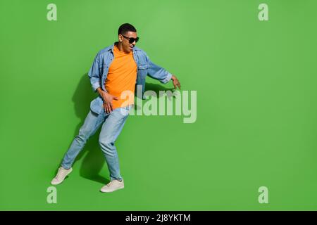 Full length image of good mood young male in sunglass dancing in nightclub isolated on green color background Stock Photo