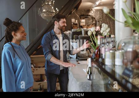 Mixed-races young couple at cafe ordering drinks and smiling. Luxury cozy place. People on date. Stock Photo