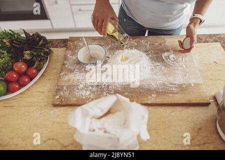 Preparation for kneading pizza dough with the addition of olive oil to flour on a kitchen board Stock Photo