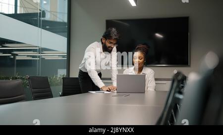 Professional Arabian Indian teacher mentor helping African woman new employee teaching intern explaining online project service corporate app using la Stock Photo