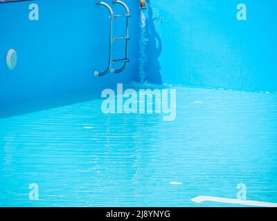 Pouring fresh water into swimming pool. Clear blue water refreshing disinfection purification, algae bacteria prevent. Summer active lifestyle, swim f Stock Photo