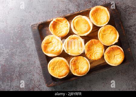 Tasty Portuguese mini Tarts Queijadas are a sweet, creamy, traditional dessert close-up on a wooden tray on the table. Horizontal top view from above Stock Photo