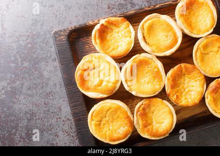 Queijadas de Sintra are sweet cheese tarts with a hint of cinnamon close-up on a wooden tray on the table. Horizontal top view from above Stock Photo