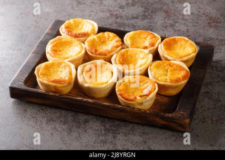 Tasty Portuguese mini Tarts Queijadas are a sweet, creamy, traditional dessert close-up on a wooden tray on the table. Horizontal Stock Photo