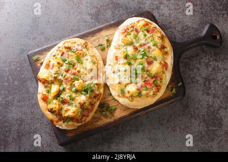 German pizza style tart flambee Swabian Dinnete with potatoes, onions and bacon close-up on a wooden board on the table. horizontal top view from abov Stock Photo