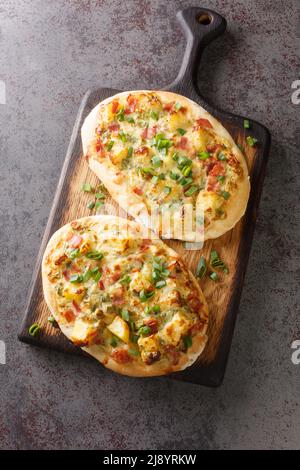 Dinnete is a traditional German dish originating from Baden-Wurttemberg is topped with sour cream, potatoes, onions, ham, and cheese close-up on a woo Stock Photo