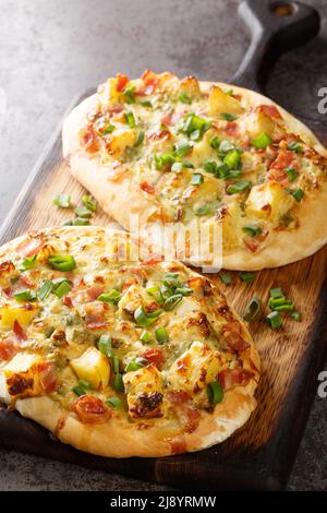 German pizza Swabian Dinnete with potatoes, onions and bacon close-up on a wooden board on the table. vertical Stock Photo