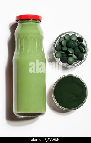 green smoothie in bottle and spirulina algae powder and pills in glass bowl on white background.useful habits,self care and healthy lifestyle concept. Stock Photo