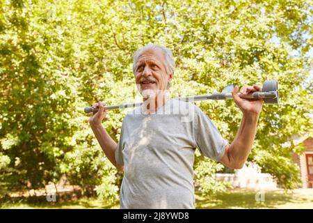 Vital senior with walking stick in rehab clinic in summer in park has fun fitness training Stock Photo