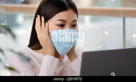 Confused asian woman in medical mask reading bad news about covid19 pandemic receive refuse email on laptop depressed stress unpleasant mistake online Stock Photo