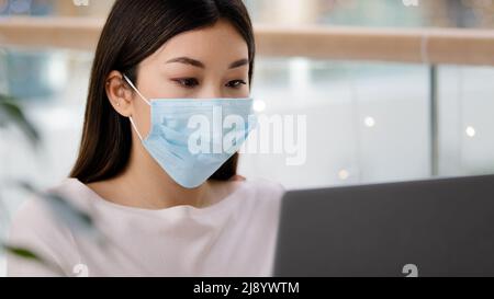Asian student Korean business woman in medical face mask freelancer writer journalist typing working laptop using free Wi-Fi studying with computer ap Stock Photo