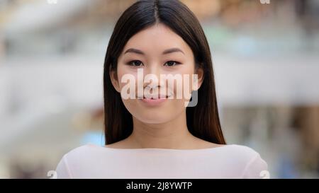 Close up female indoors headshot Asian happy smiling millennial girl. 20s brunette woman model lady with natural make-up face cosmetology service. Bus