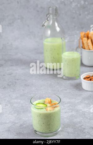 Chilled cucumber soup with nuts, herbs, yogurt, crackers in a glass beaker on a gray background. healthy vegan food Stock Photo