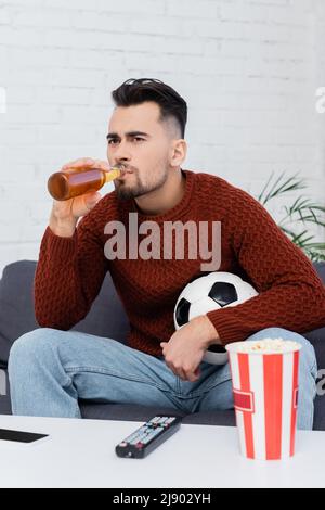 focused football fan drinking beer while watching game on tv at home Stock Photo