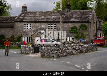 Conistone village centre (attractive stone properties, road junction, person walking, signpost pointing) - Wharfedale, Yorkshire Dales, England, UK.