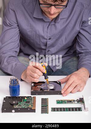 The master repairs the disassembled hard disk on the desktop next to the RAM modules, the board and tools Stock Photo