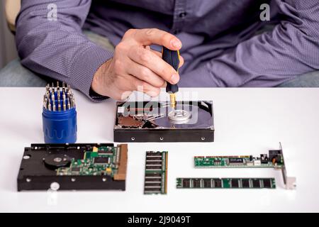 The master repairs the disassembled hard disk on the desktop next to the RAM modules, the board and tools Stock Photo