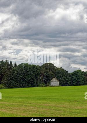 An Old well preserved Doocot or Dovecote situated in a field of newly sown wheat with a mixed woodland behind and dark clouds above. Stock Photo