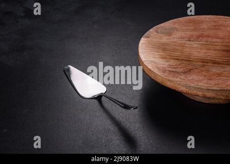 A metal cake blade with an empty brown cake stand on a dark concrete background. Preparing a festive table Stock Photo