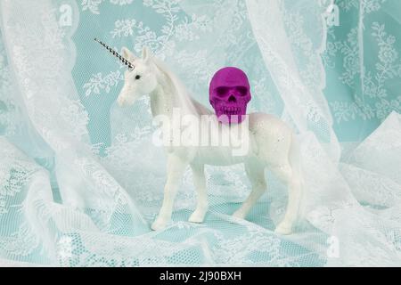 a shiny white unicorn carrying a plastic skull on its back. Minimal and creative color still life photography Stock Photo
