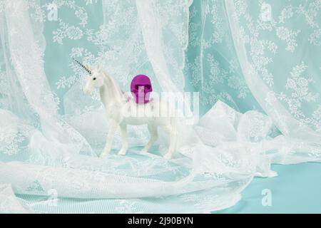 a shiny white unicorn carrying a plastic skull on its back. Minimal and creative color still life photography Stock Photo