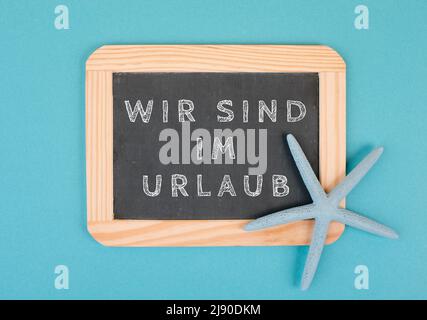 We are on vacation is standing in german language on the chalkboard with a sea star, holiday background, time out in summer, hot weather, advertising Stock Photo