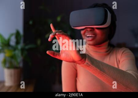 Joyful afro female touching virtual object with finger while working in virtual reality headset Stock Photo