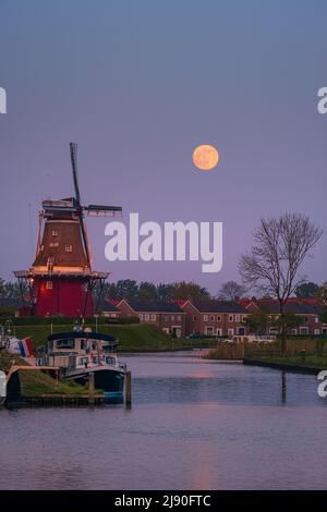 Sunset and moonrise with a full moon near Flour Mill "De Hoop" in the Dutch town of Dokkum, in the province of Friesland in the northern part of the N Stock Photo
