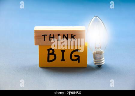 Think big text on wooden blocks with shining bulb on light blue background. Motivational concept Stock Photo
