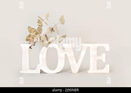 Love word made with wooden letters and eucalyptus branches with leaves on a gray background Stock Photo