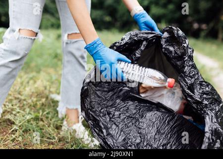 Young millennial caucasian woman cleaning-up public park or forest of plastic garbage. Volunteer picking up plastic bottle in woods. Green and clean Stock Photo