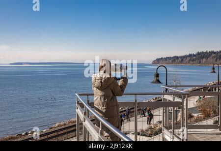Young Beautiful woman On A Pier Near The Sea Looks Through Binoculars On. Travel Search Journey Concept. Young girl looking through telescopes at the Stock Photo