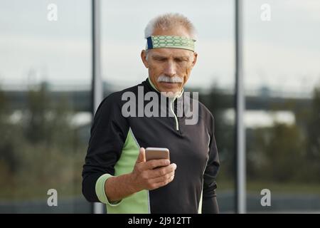 Horizontal waist up portrait of modern senior man wearing tracksuit using his smartphone Stock Photo