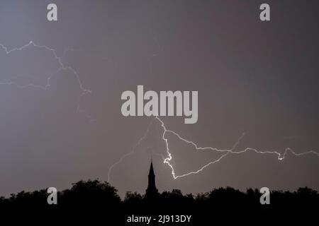 Rain falling and stroke of forked lightning during thunderstorm at night over church tower and trees Stock Photo
