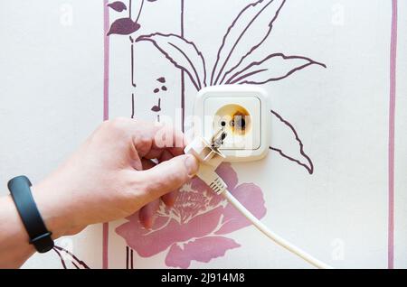 The plug and socket are burnt, the man is holding the burnt socket. Short circuit, fire, danger Stock Photo