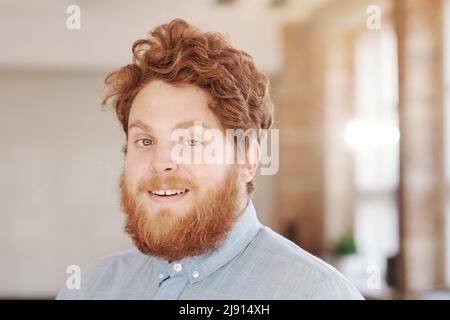 Portrait of smiling young red bearded man with curly hair standing in office of modern company Stock Photo
