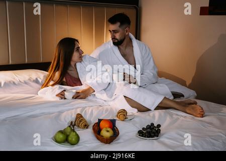 Happy young couple sitting in bed in morning and having breakfast Stock Photo