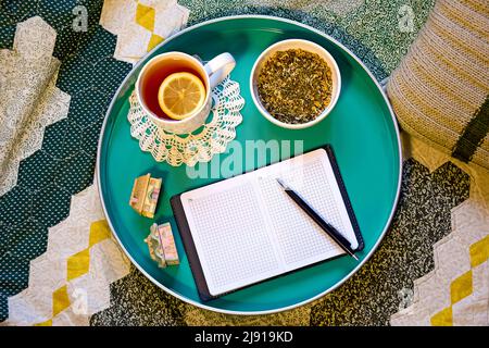 Cup of tea with lemon, natural herbal tea and a notebook with pen on green tray, rustic lifestyle. Top view. Flat lay. Stock Photo
