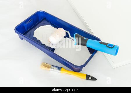Painter's utensils. Roller, brush and tray with white paint in interior work area. Copy space. Stock Photo