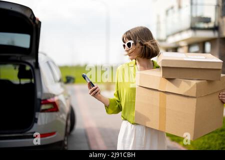 Woman using phone while standing with parcels on a street outdoors Stock Photo