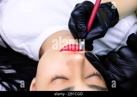 The tattoo master draws a sketch on the model's lips with a pen Stock Photo