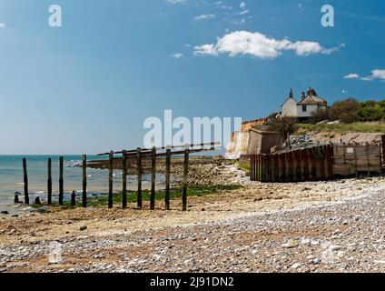 Beach at Cuckmere Haven near Seaford showing erosion of the cliffs and remains of sea defences with old coastguard cottages on the cliff edge. Stock Photo