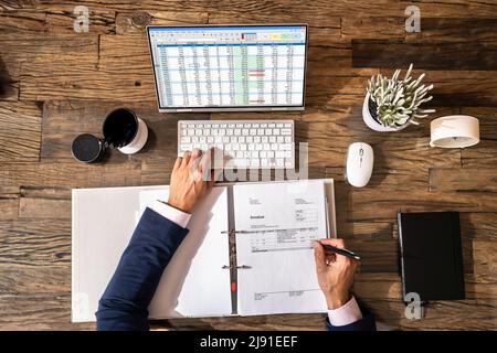 Looking At Invoice And Spreadsheet On Computer At Work Stock Photo