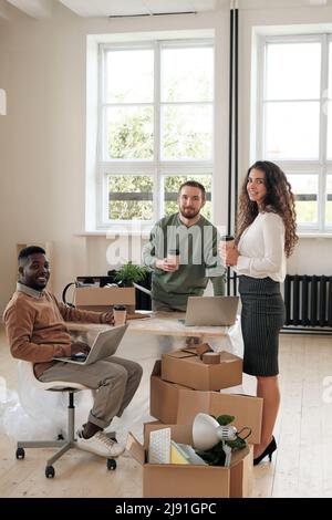 Team of smiling young multi-ethnic specialists drinking coffee and discussing new promotion campaign in new office after renovation Stock Photo